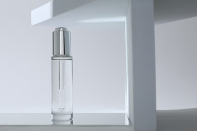 Bottle of serum on mirror surface against light background