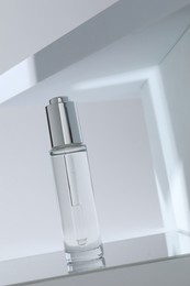 Photo of Bottle of serum on mirror surface against light background, low angle view