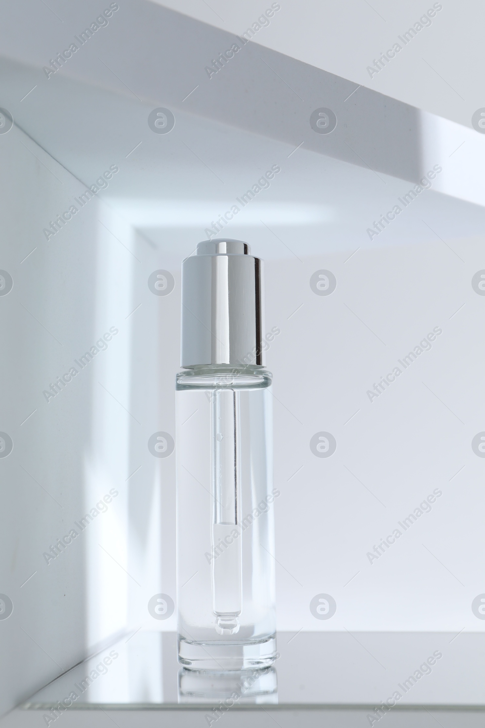 Photo of Bottle of serum on mirror surface against light background