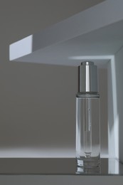 Bottle of serum on mirror surface against grey background