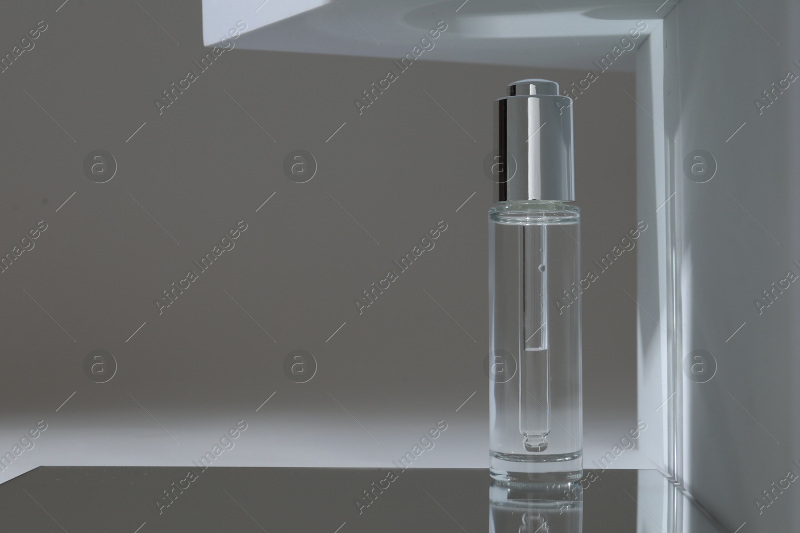 Photo of Bottle of serum on mirror surface against grey background. Space for text