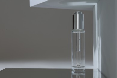 Bottle of serum on mirror surface against grey background. Space for text