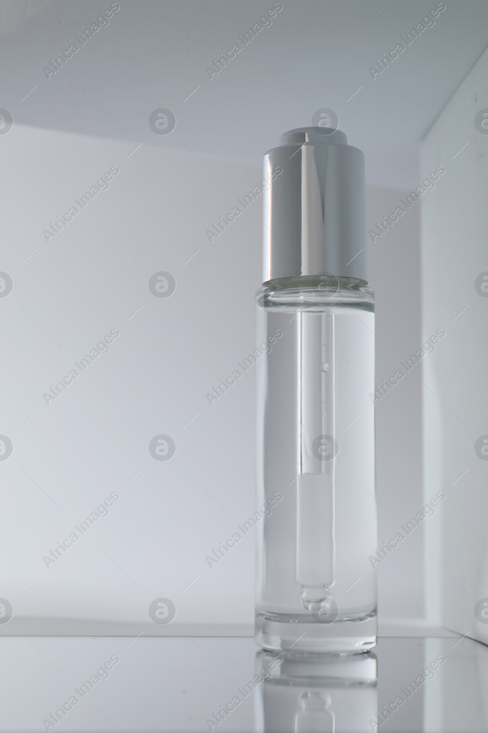 Photo of Bottle of serum on mirror surface against grey background