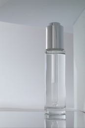 Bottle of serum on mirror surface against grey background