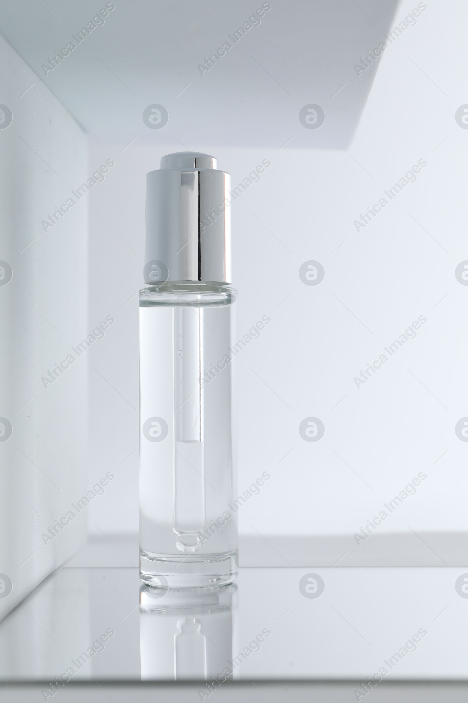 Photo of Bottle of serum on mirror surface against light background