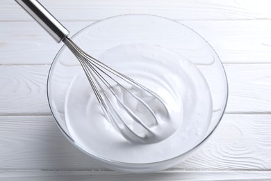 Photo of Whisk and whipped cream in bowl on white wooden table