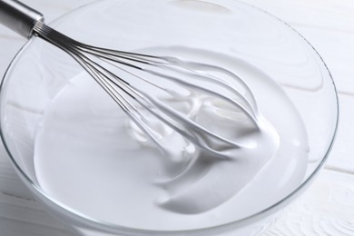 Photo of Whisk and whipped cream in bowl on white wooden table, closeup