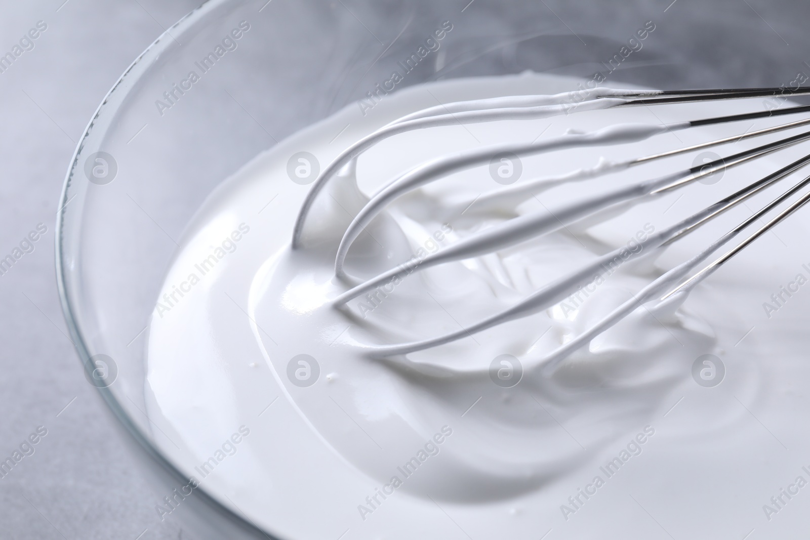 Photo of Whisk and whipped cream in bowl on grey table, closeup