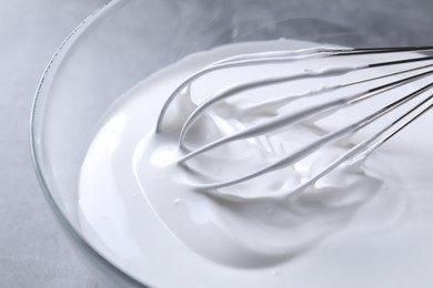 Photo of Whisk and whipped cream in bowl on grey table, closeup