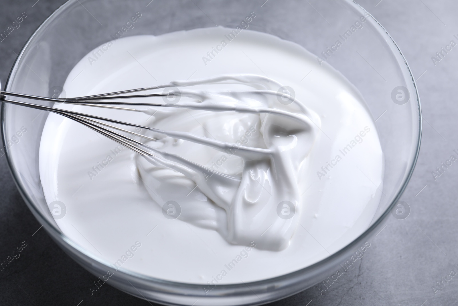 Photo of Whisk and whipped cream in bowl on grey table, closeup