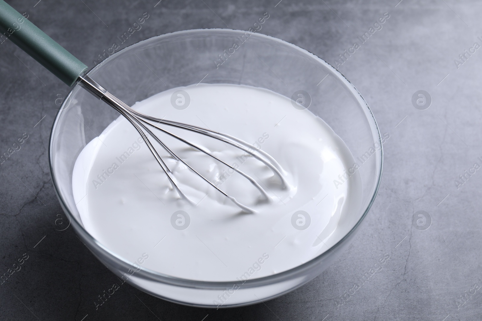 Photo of Whisk and whipped cream in bowl on grey table