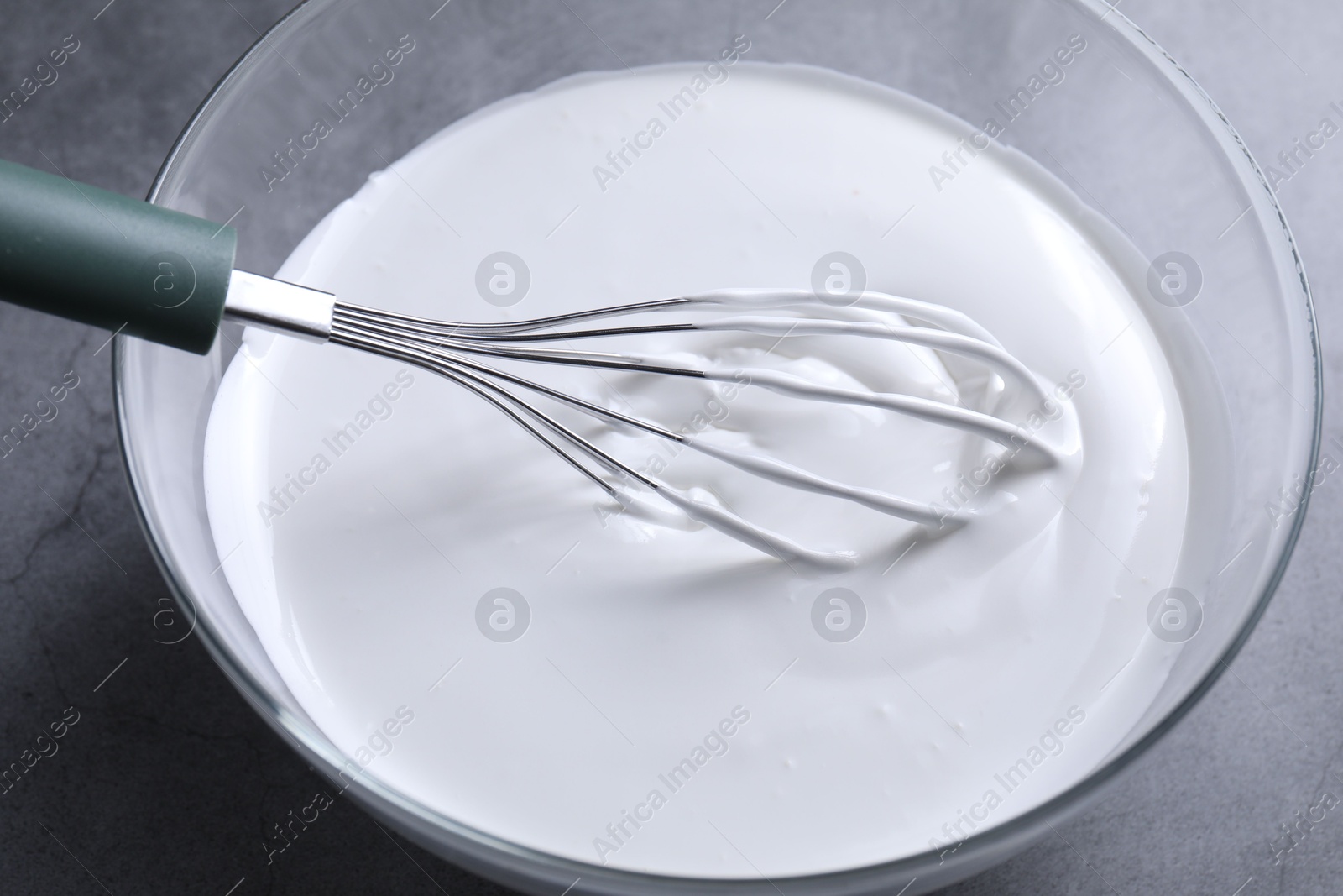 Photo of Whisk and whipped cream in bowl on grey table, closeup