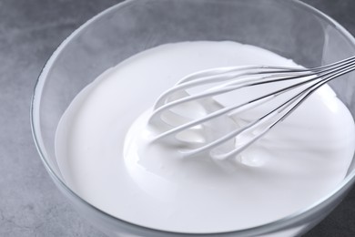 Photo of Whisk and whipped cream in bowl on grey table, closeup