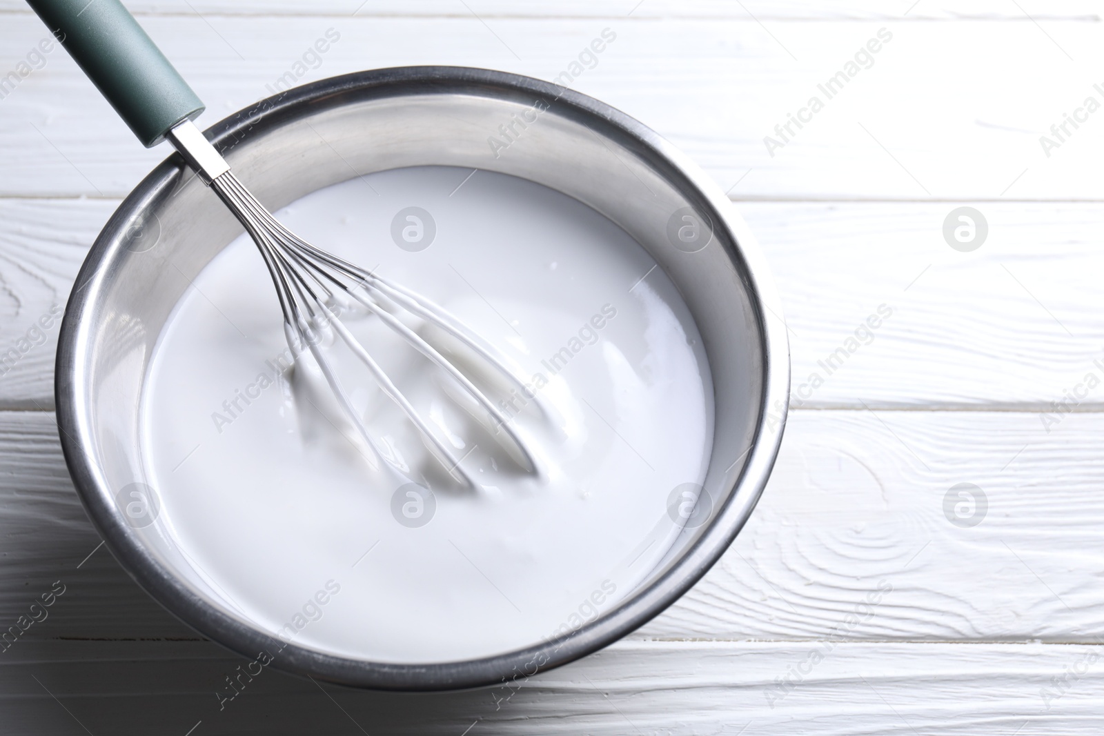 Photo of Whisk and whipped cream in bowl on white wooden table