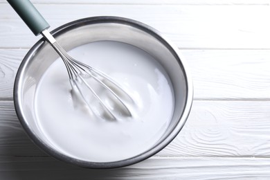 Photo of Whisk and whipped cream in bowl on white wooden table