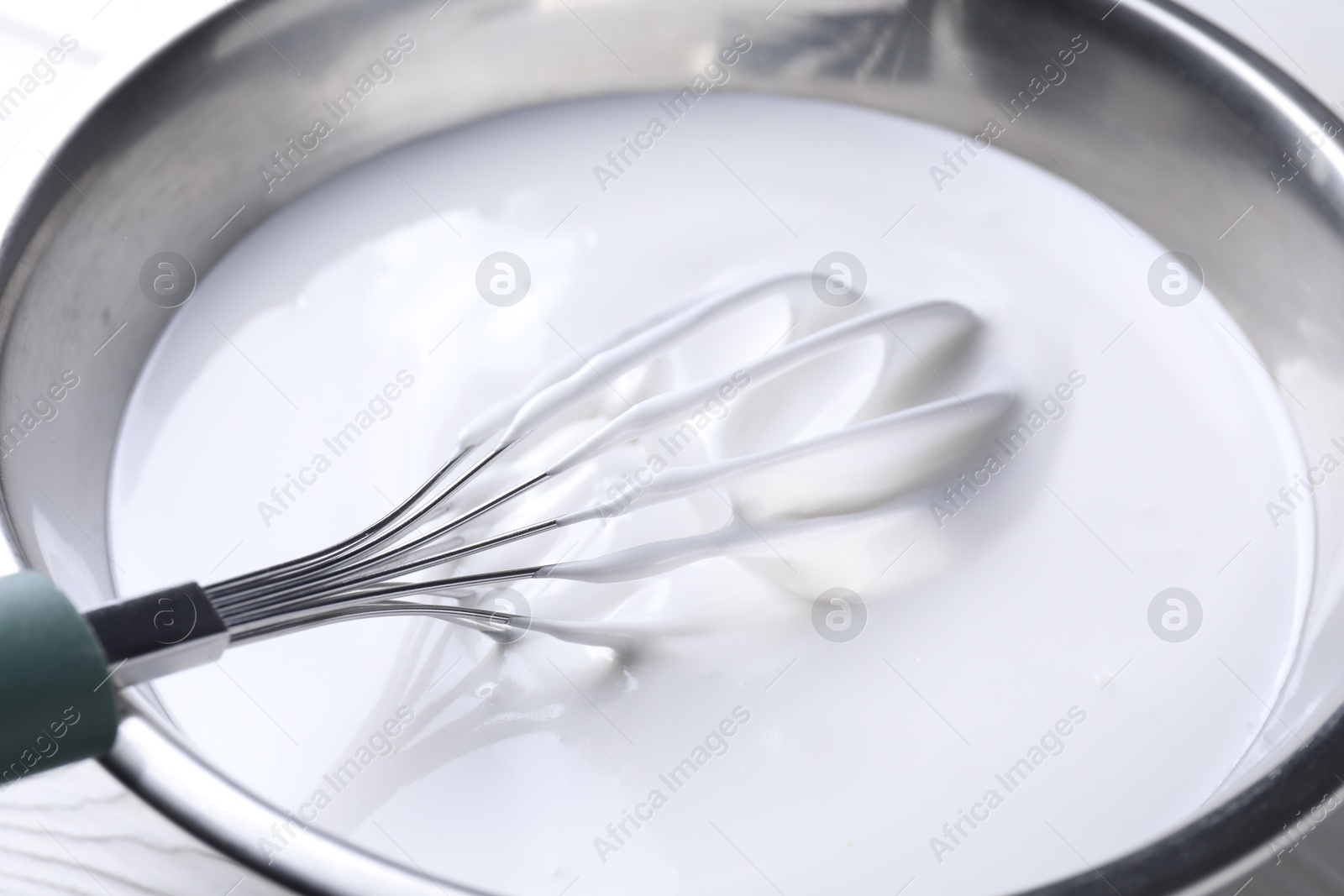 Photo of Whisk and whipped cream in bowl on white table, closeup