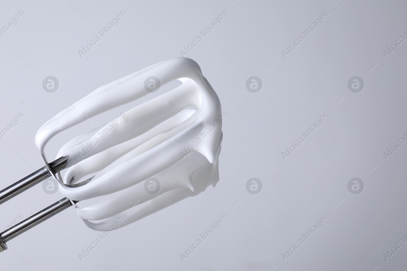 Photo of Whisks with whipped cream on white background, closeup. Space for text