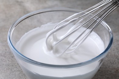 Photo of Whisking whipped cream in bowl on grey table, closeup