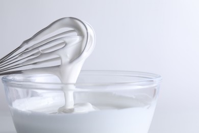 Photo of Whisk and bowl with whipped cream on white background, closeup