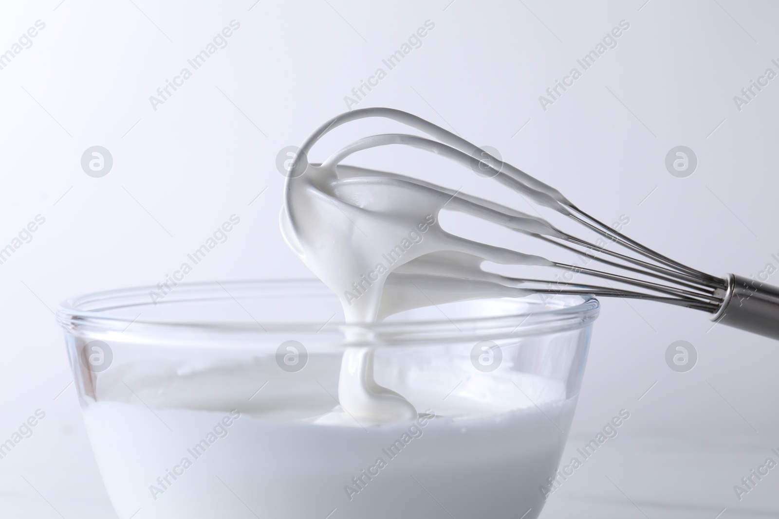 Photo of Whisk and bowl with whipped cream on white background, closeup