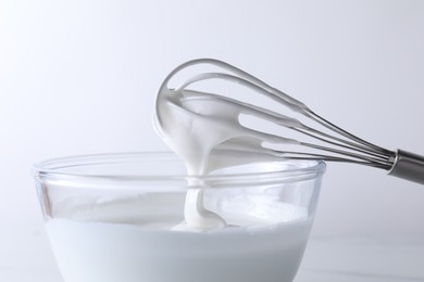 Photo of Whisk and bowl with whipped cream on white background, closeup