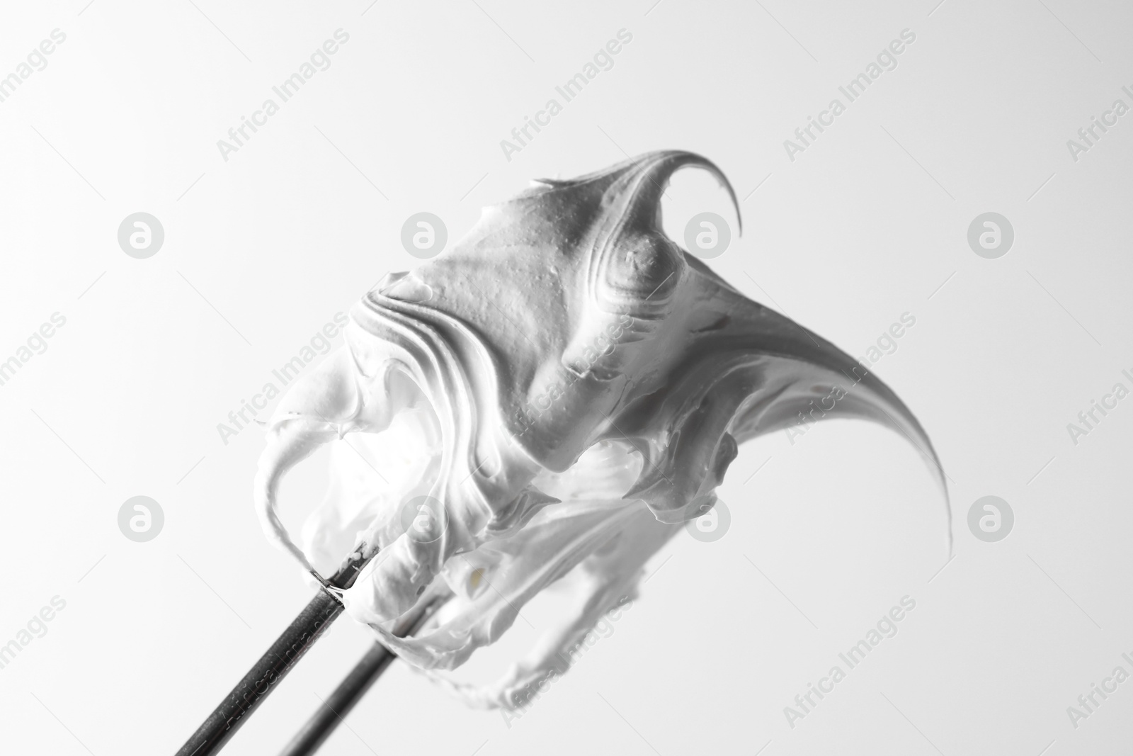 Photo of Whisk with whipped cream on white background, closeup