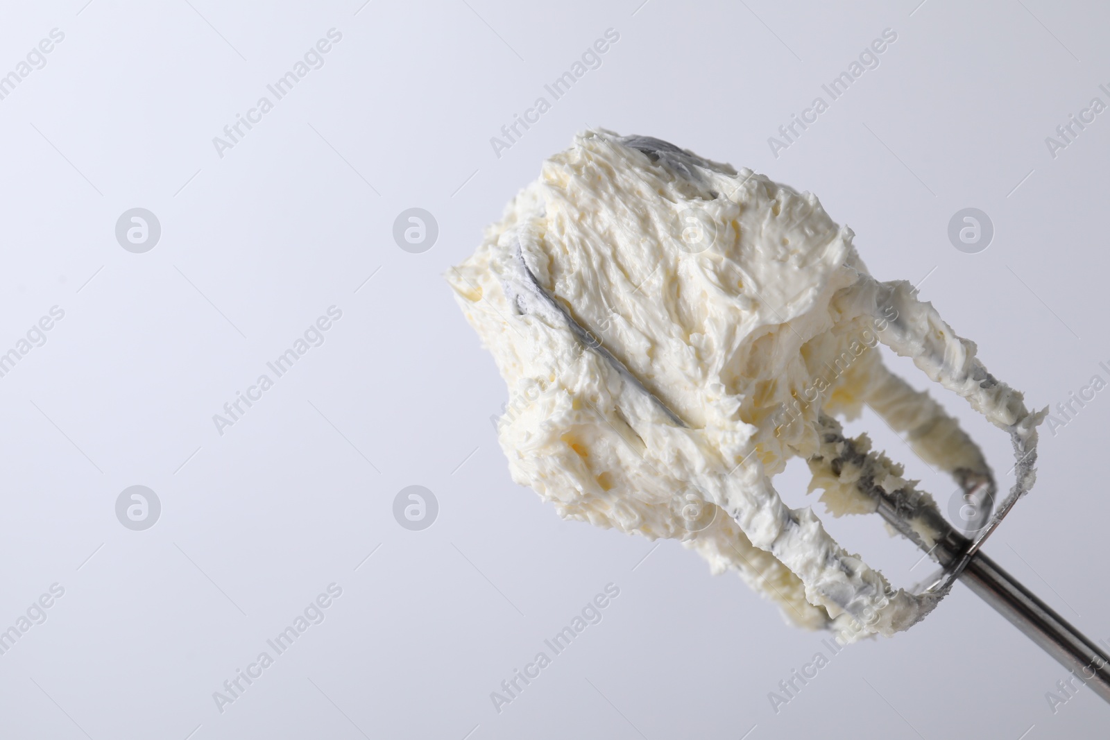 Photo of Whisk with whipped cream on white background, closeup. Space for text