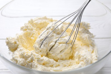 Photo of Bowl with whisk and whipped cream on white wooden table, closeup