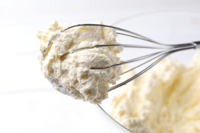 Photo of Bowl with whisk and whipped cream on white table, closeup