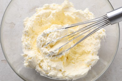 Photo of Bowl with whisk and whipped cream on light grey table, top view