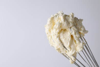 Photo of Whisk with whipped cream on white background, closeup. Space for text