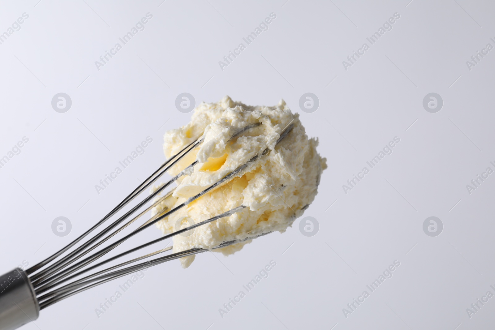 Photo of Whisk with whipped cream on white background, closeup. Space for text