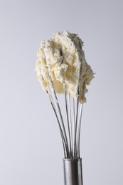 Photo of Whisk with whipped cream on white background, closeup