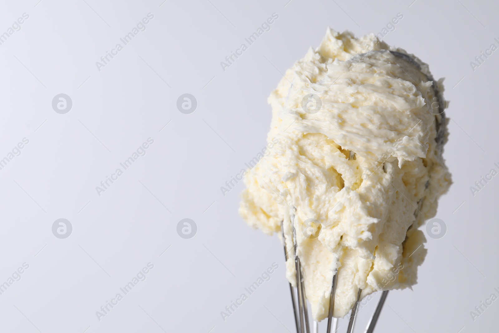 Photo of Whisk with whipped cream on white background, closeup. Space for text