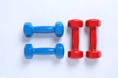 Photo of Blue and red dumbbells on white background, flat lay. Sports equipment