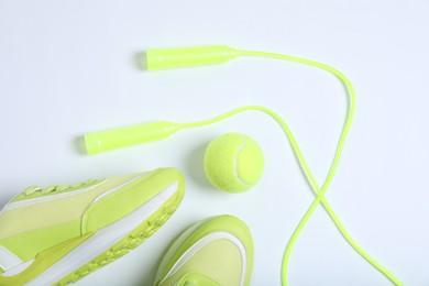 Photo of Sneakers, skipping rope and tennis ball on white background, flat lay. Sports equipment