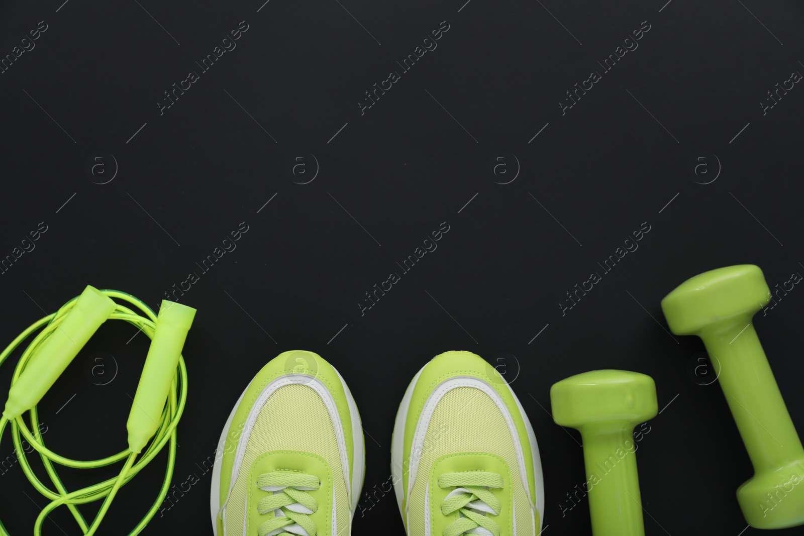 Photo of Sneakers, dumbbells and skipping rope on black background, flat lay with space for text. Sports equipment