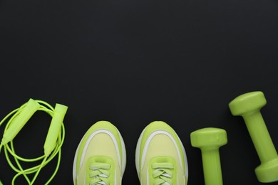 Photo of Sneakers, dumbbells and skipping rope on black background, flat lay with space for text. Sports equipment