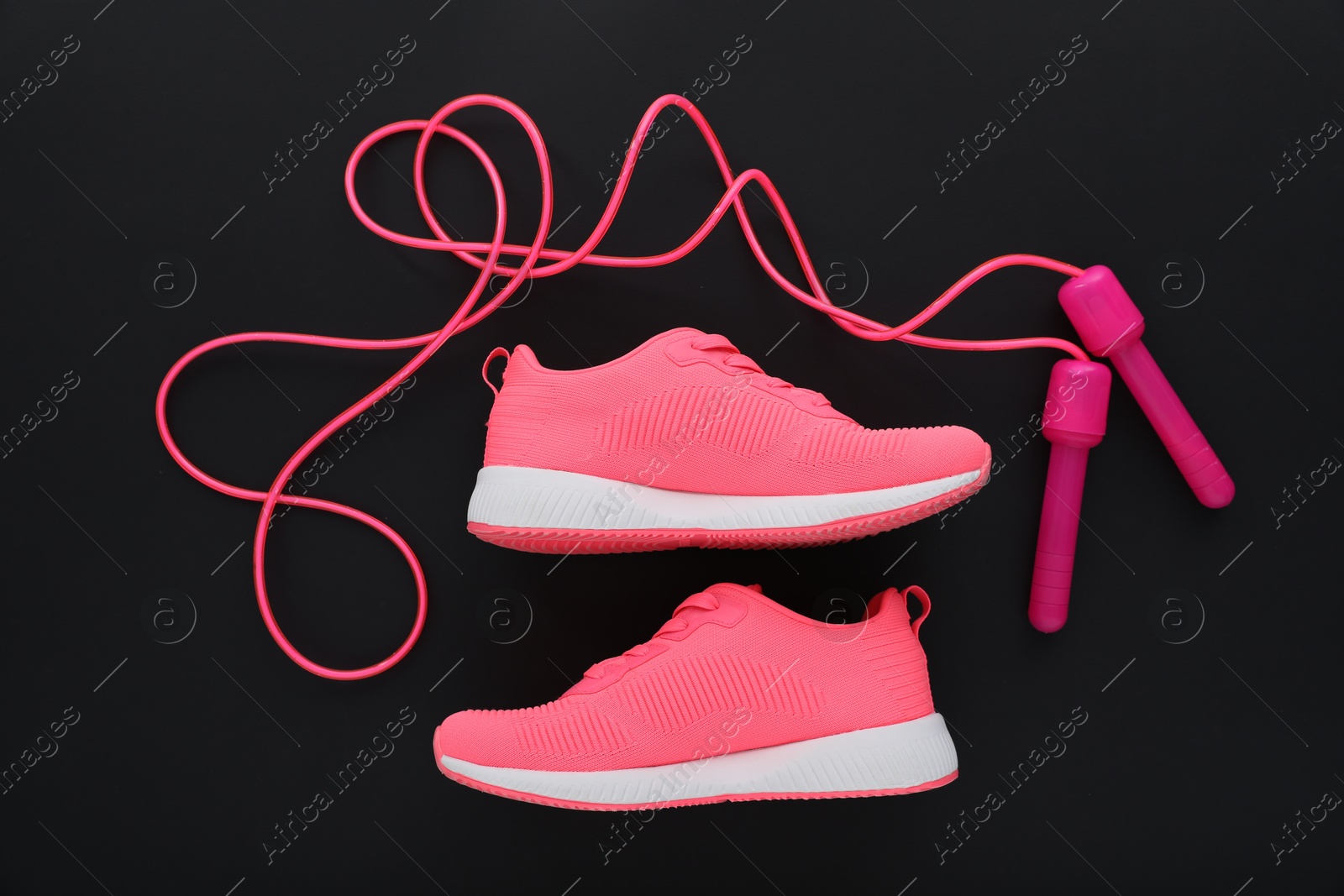 Photo of Sneakers and skipping rope on black background, flat lay. Sports equipment