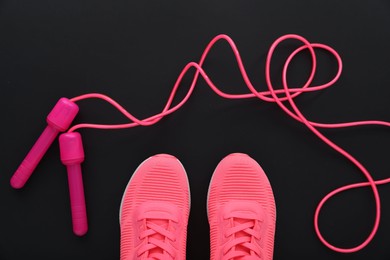 Photo of Sneakers and skipping rope on black background, flat lay. Sports equipment