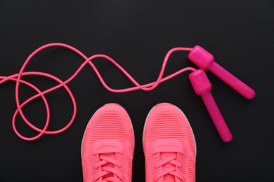 Photo of Sneakers and skipping rope on black background, flat lay. Sports equipment