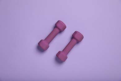 Photo of Purple dumbbells on violet background, top view. Sports equipment