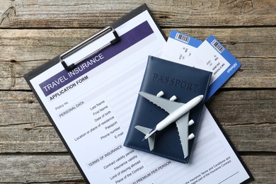 Photo of Medical tourism. Travel insurance application form, plane model, passport and flight tickets on wooden table, top view