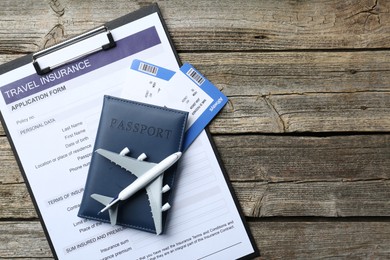 Photo of Medical tourism. Travel insurance application form, plane model, passport and flight tickets on wooden table, top view. Space for text