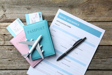 Photo of Medical tourism. Travel insurance application form, plane model, passports, flight tickets and pen on wooden table, flat lay