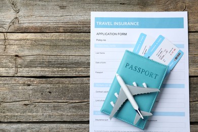 Photo of Medical tourism. Travel insurance application form, plane model, passport and flight tickets on wooden table, top view. Space for text