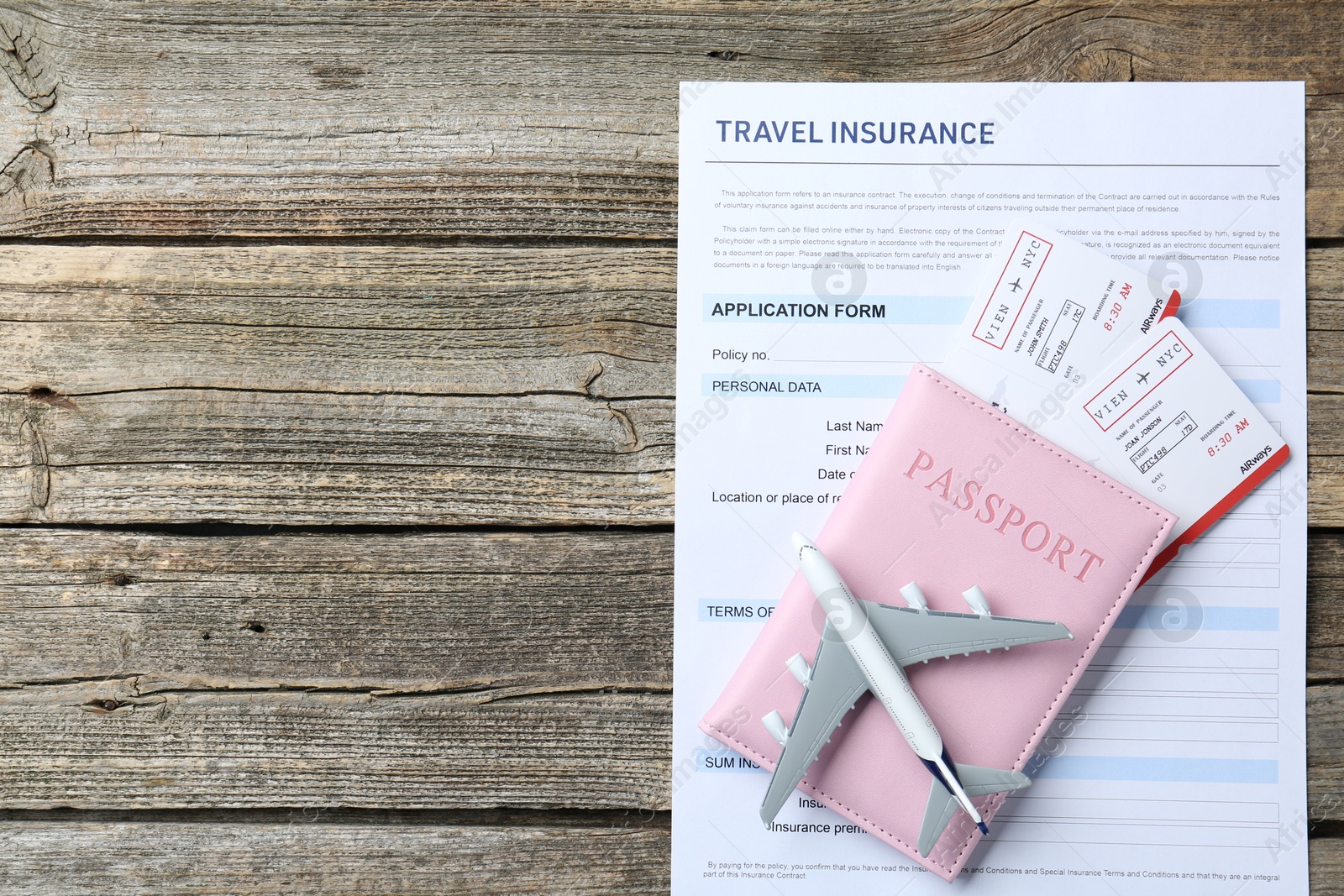 Photo of Medical tourism. Travel insurance application form, plane model, passport and flight tickets on wooden table, top view. Space for text