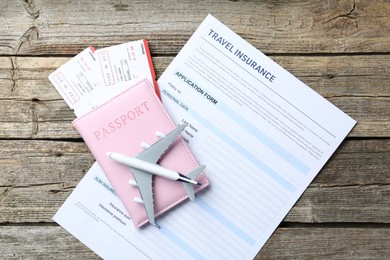 Photo of Medical tourism. Travel insurance application form, plane model, passport and flight tickets on wooden table, top view