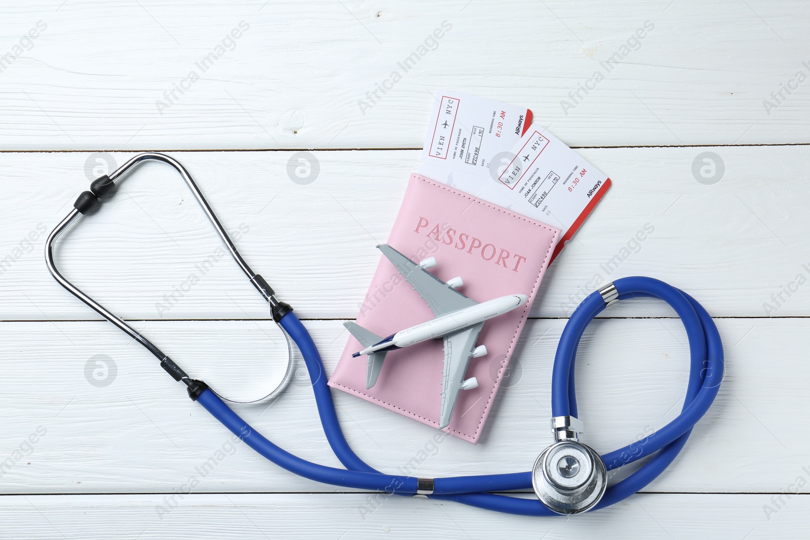 Photo of Medical tourism. Stethoscope, plane model, passport and flight tickets on white wooden table, flat lay