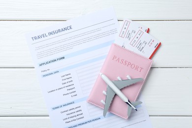 Photo of Medical tourism. Travel insurance application form, plane model, passport and flight tickets on white wooden table, top view